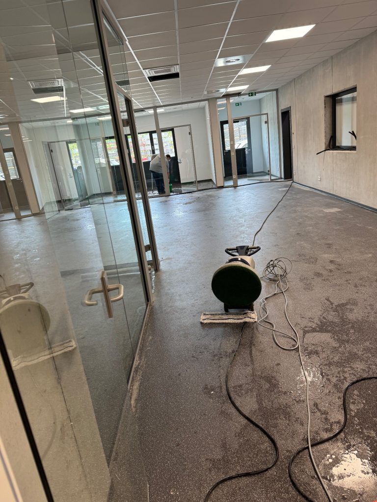 Maschinelle Bodenreinigung im Büro – Baufeinreinigung Professionelle maschinelle Bodenreinigung mit einer Einscheibenmaschine in einem leeren, neuen Bürogebäude mit modernen Glaswänden.