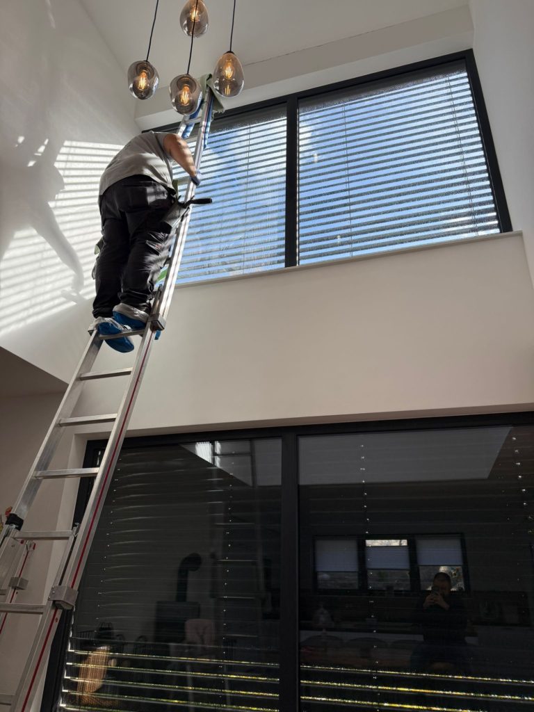 Glasreinigung im Innenbereich Fensterreiniger auf einer hohen Leiter putzt große Dachfenster und Festverglasungen im Innenbereich eines Hauses in Rottenburg.