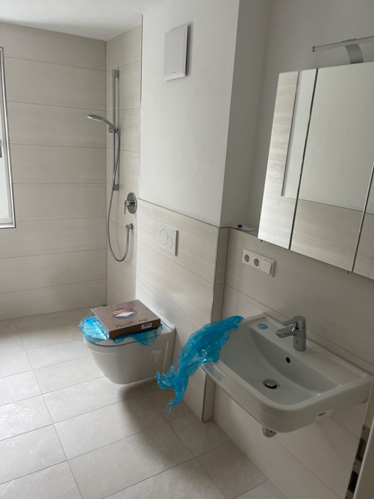 Vor-Zustand: Badezimmer mit Baustaub vor der Reinigung Unbereinigtes, modernes Badezimmer im Neubau vor der Bauschlussreinigung, mit Baustaub und Rückständen an Fliesen und Sanitärobjekten.