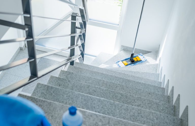 Blick auf eine Treppe mit einem Wischmopp und einem Reinigungsmittel in der Nähe.